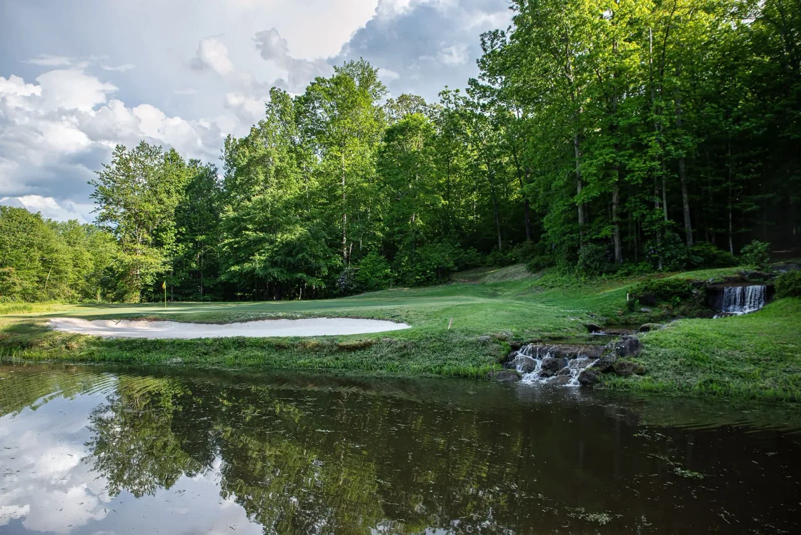 Scenic view of a lush green golf course hole, sand bunker, and small waterfall pond at Cherokee Valley, SC.
