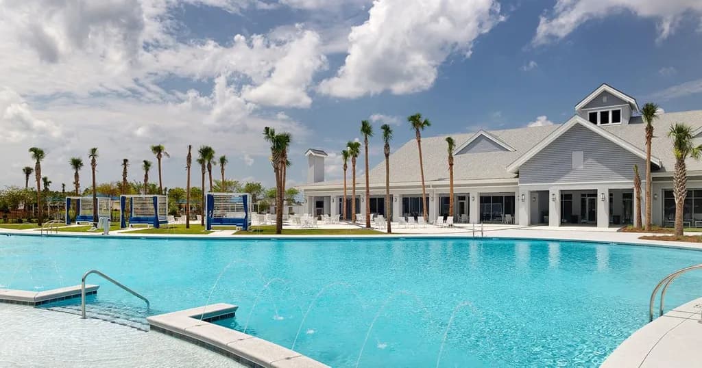 Outdoor swimming pool with water features and cabanas in front of a clubhouse at Del Webb Greenville.