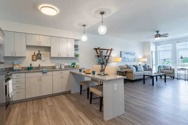 Open concept kitchen and living area with light wood cabinetry, stone island, and comfortable seating at Merrill Gardens.