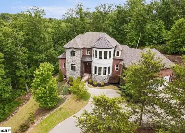 Aerial view of a luxury brick and stone home with a turret, nestled on a heavily wooded lot in Montebello, Greenville.