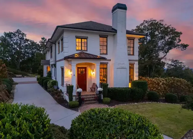 Two-story white brick home with a red door and manicured landscaping in Montebello, Greenville, SC at sunset.