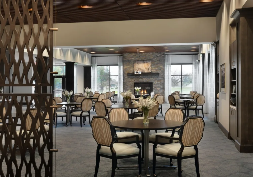 Dining area at Rolling Green Village in Greenville with tables, chairs, and a stone fireplace.